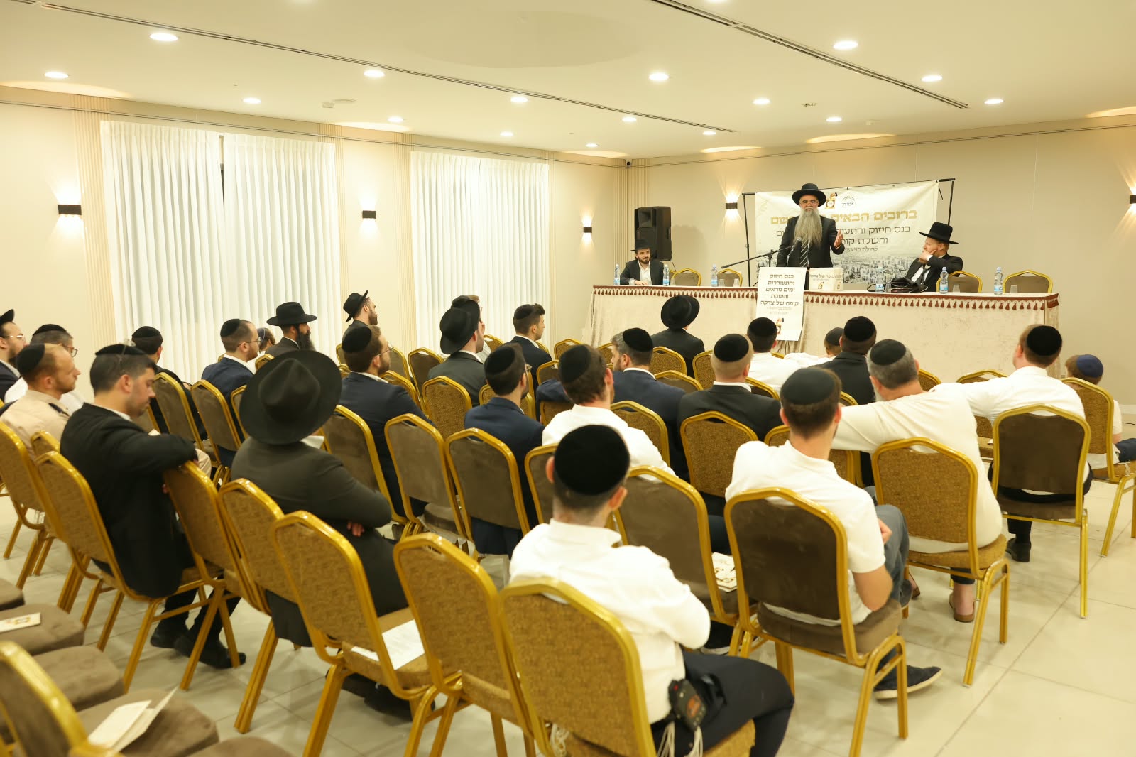 מבט מאחורי האולם על הקהל היושב מול שולחן הכבוד